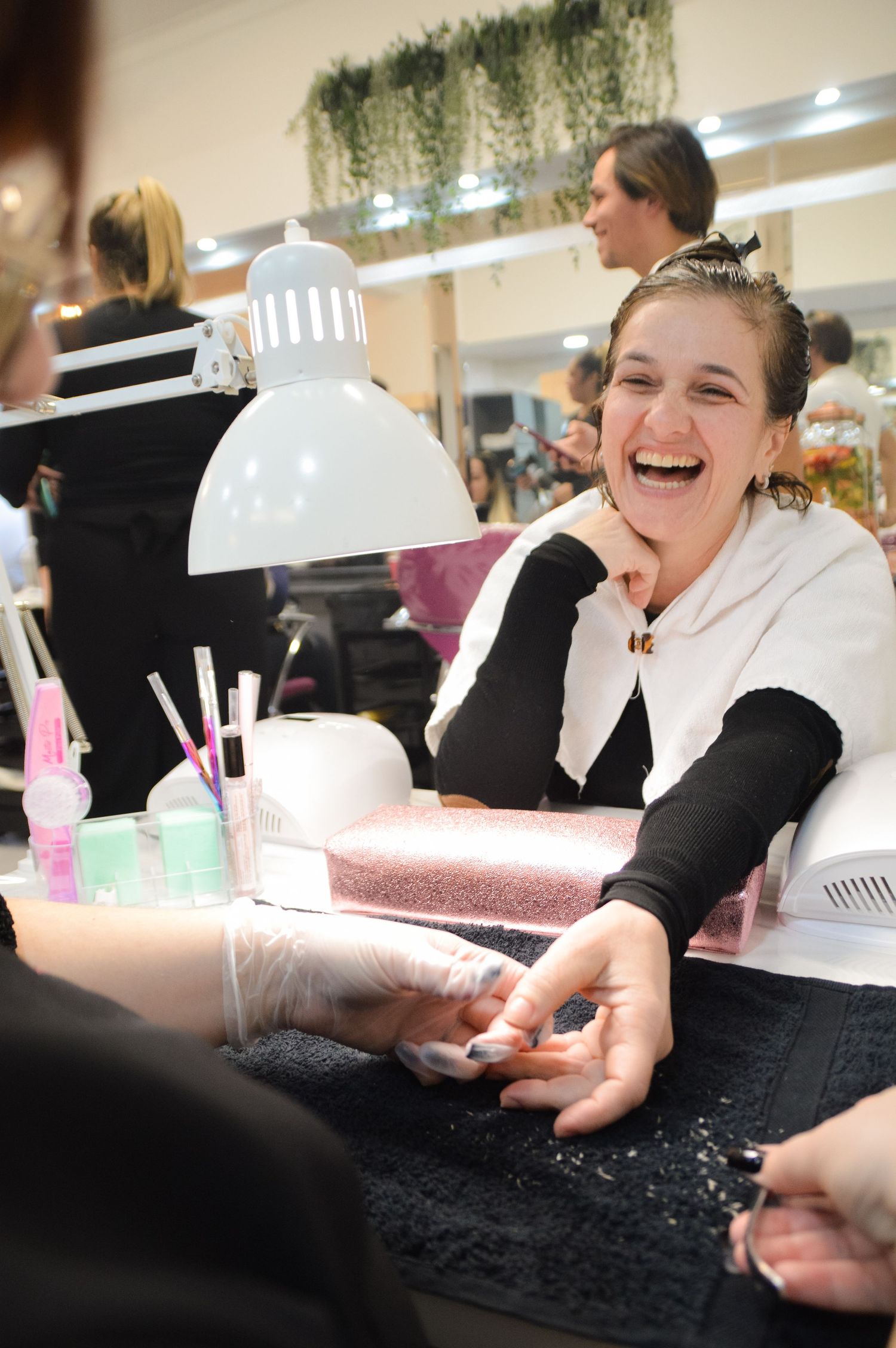 Someone laughing during a manicure session at a nail salon with beauty supplies visible on the table.