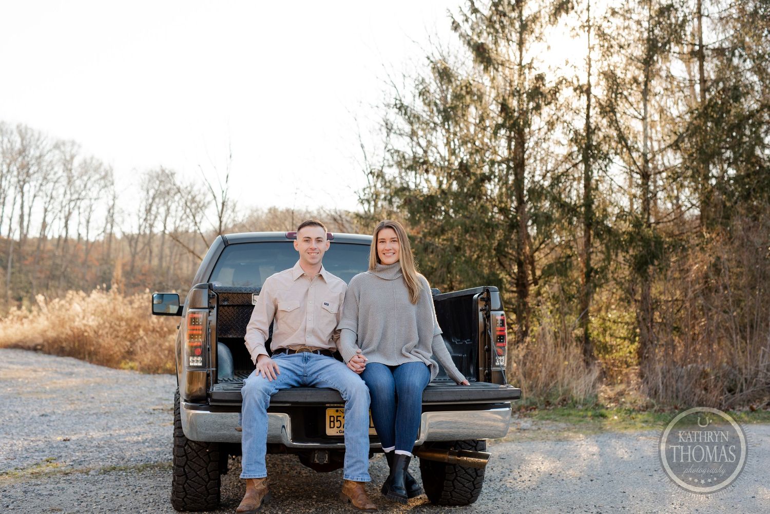 Young couple in matching casual outfits sitting together on a pickup truck tailgate.