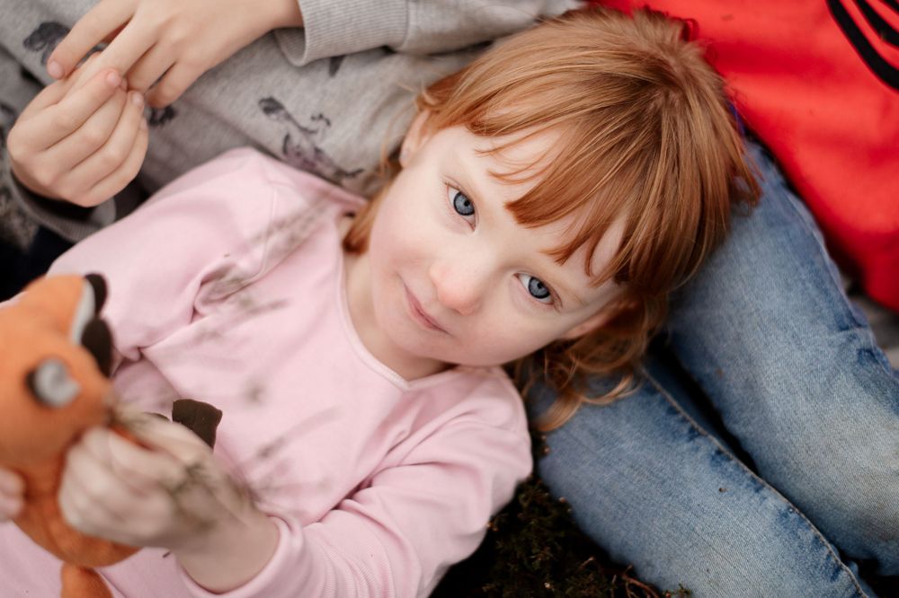 Child in pink sweater lying down with a playful expression.