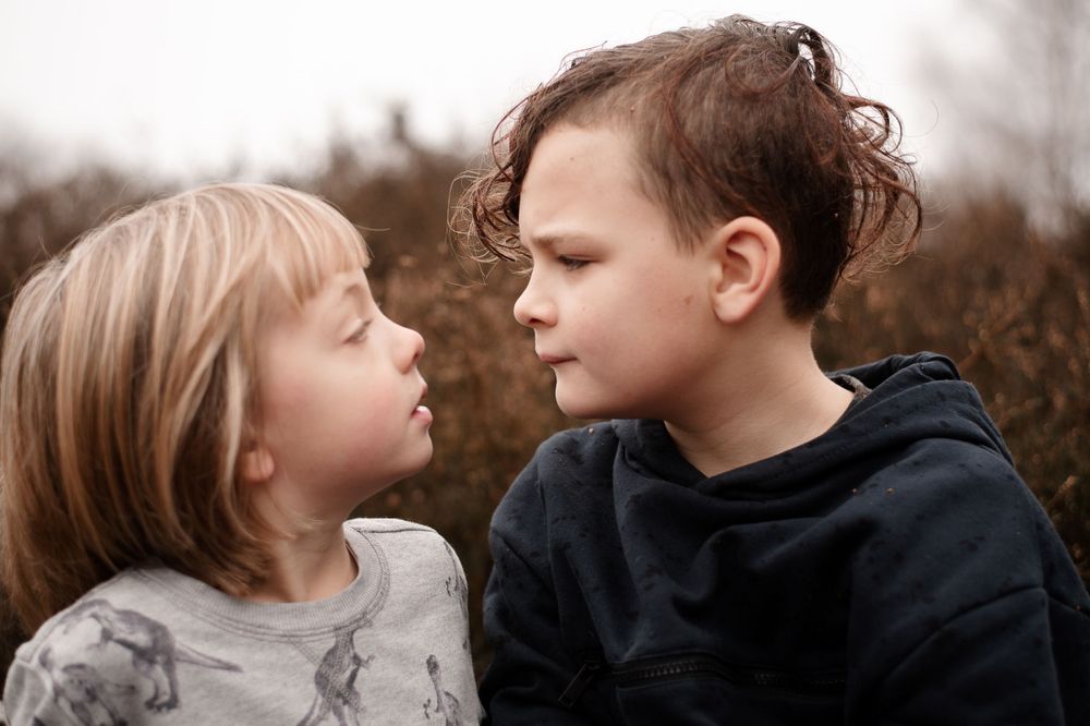 Two young children with contrasting expressions facing each other in a moody outdoor setting.
