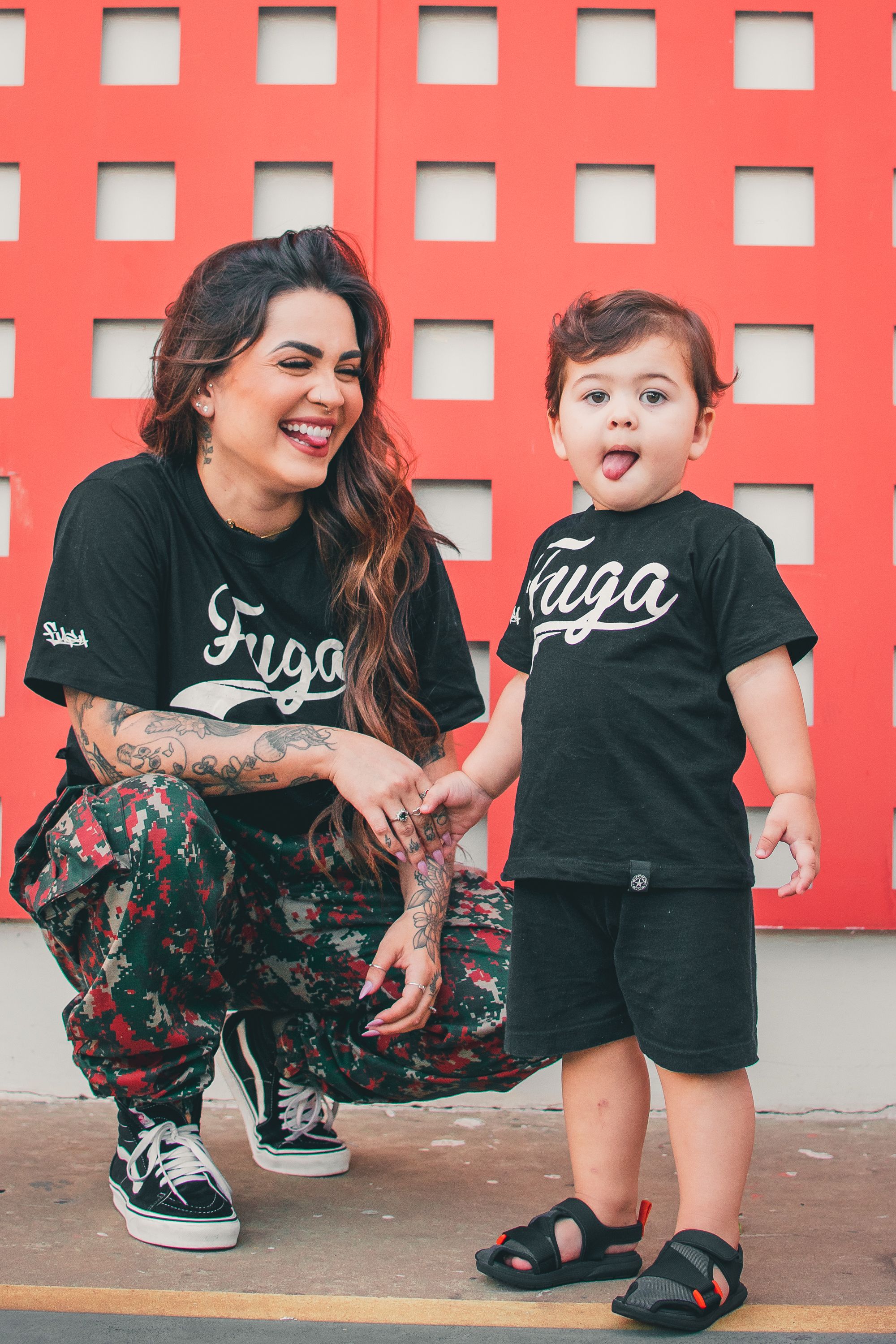 Sweet moments captured against a vibrant red wall with matching black outfits.