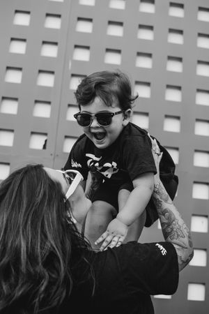 Black and white photo of playful moment between parent and child wearing sunglasses against geometric wall.
