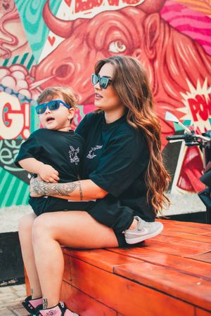 Parent and child in matching outfits pose against colorful graffiti wall on red bench.