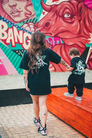 Matching black t-shirts shown from behind against colorful street art mural with red bull design.