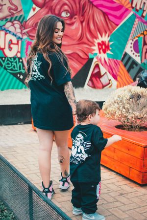 Mother and child wearing matching black outfits pose in front of colorful street art mural.
