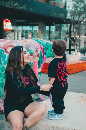 Parent and toddler in coordinating black outfits share a moment by vibrant graffiti wall.