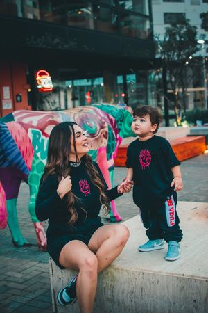 Adult and child in matching black clothing interact playfully near urban street art.