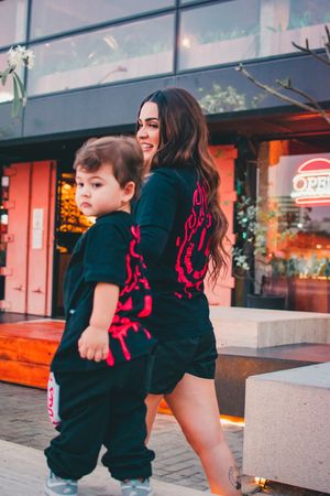 Side view of adult and child in matching dark outfits with red graphic designs.