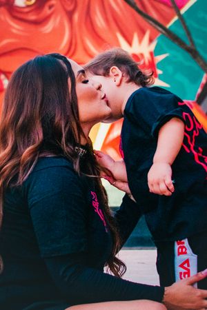 Sweet moment captured between parent and child in matching outfits against colorful backdrop.