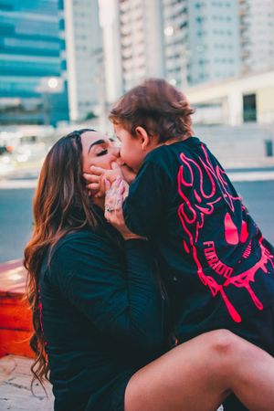 Two people wearing dark clothing share an intimate moment in front of an urban backdrop.