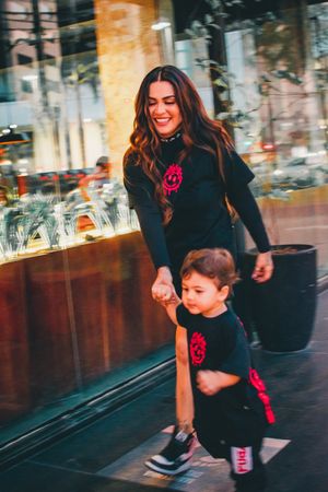 Parent and child wearing matching black outfits walking together on a city street.