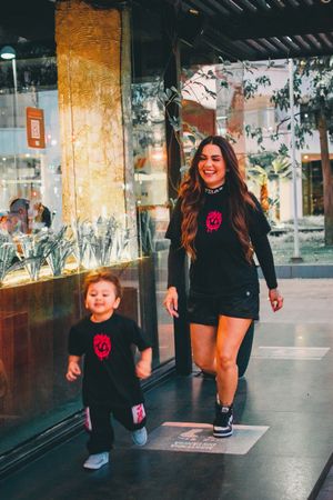Adult and child in coordinated dark outfits walking together past storefronts.