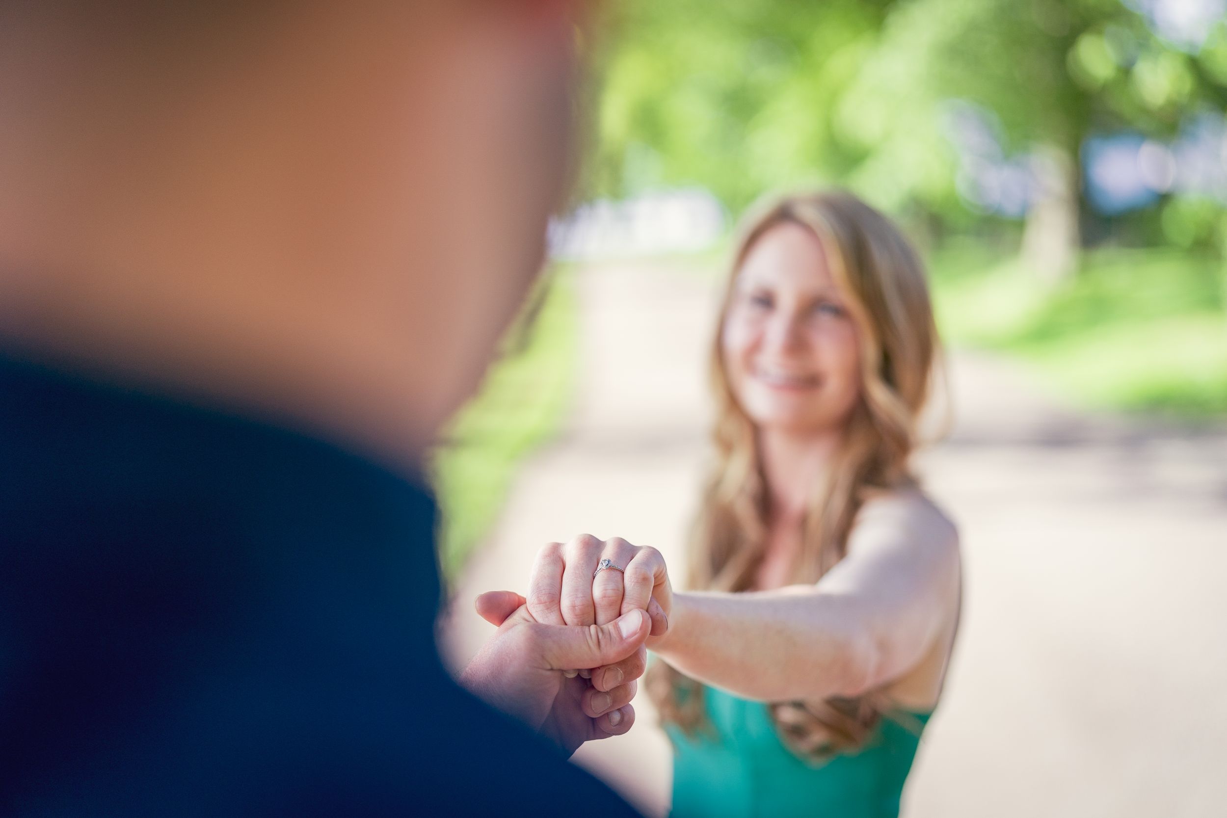 Engagement photo shoot in the spring. The future groom hold his fiancee's hand looking at the engagement ring.