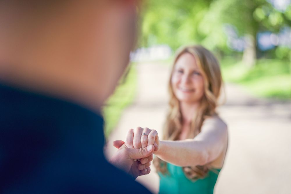 Engagement photo shoot in the spring. The future groom hold his fiancee's hand looking at the engagement ring.