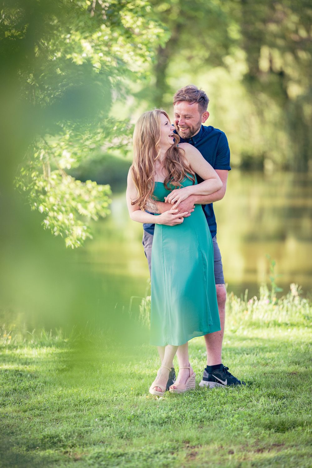 Couple enjoying a hug in the garden. Her green dress blends with the garden's spring colours and complements the engagement's ring stone
