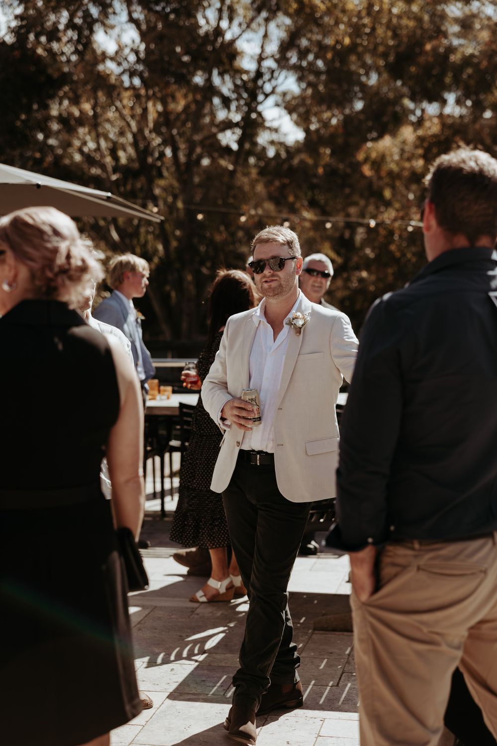 Wedding guests socialize on wooden deck during daytime celebration.