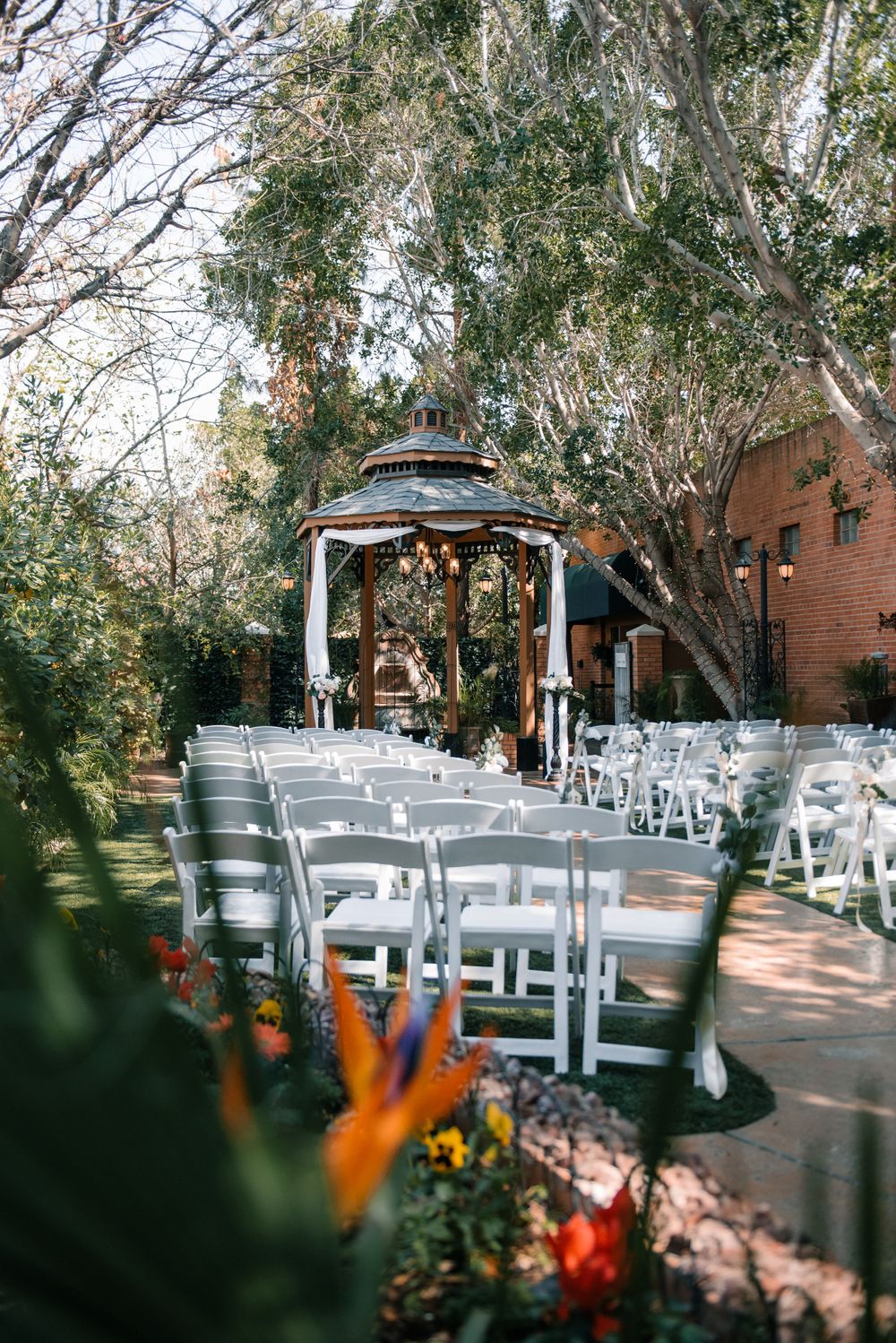 White folding chairs arranged for an outdoor wedding ceremony under trees with string lights.