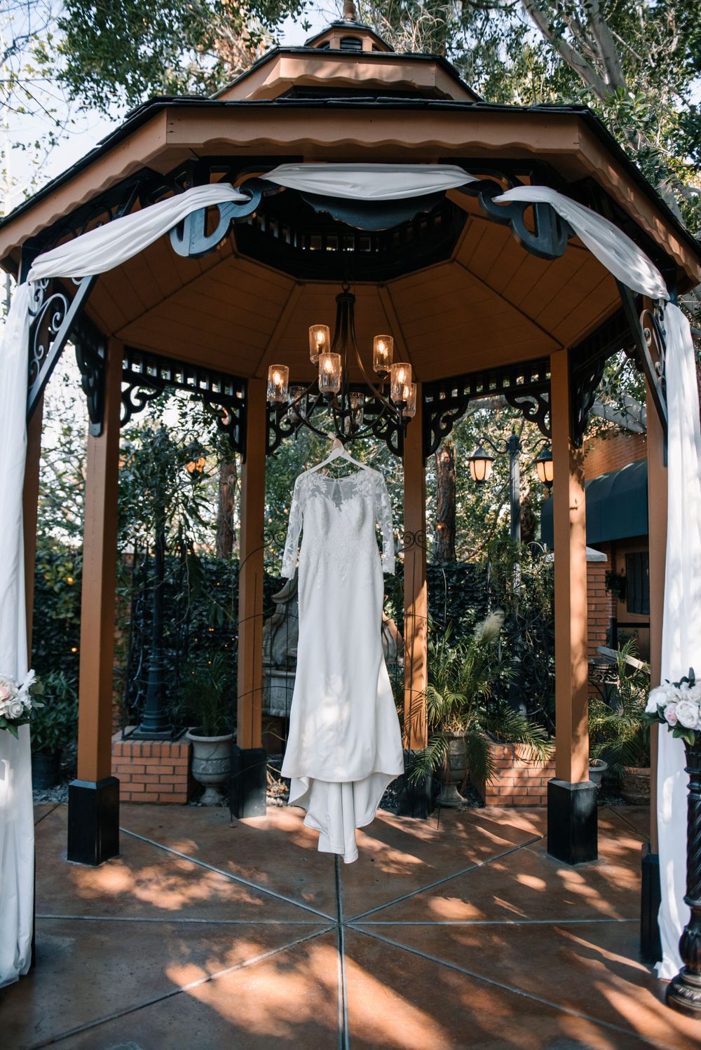 A wedding dress displayed in a wooden gazebo with string lights and white draping.