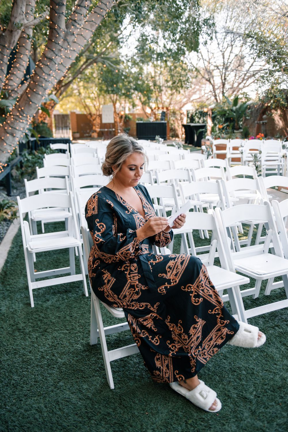 A guest in a patterned dress sits among white chairs at an outdoor wedding venue.