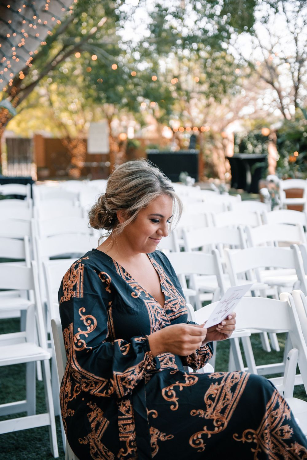 A wedding guest checks their phone while seated in rows of white ceremony chairs.