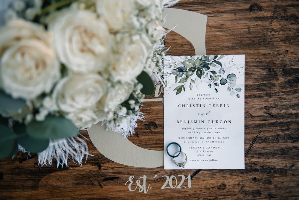 Elegant white floral wedding invitation with greenery details displayed on wooden surface.