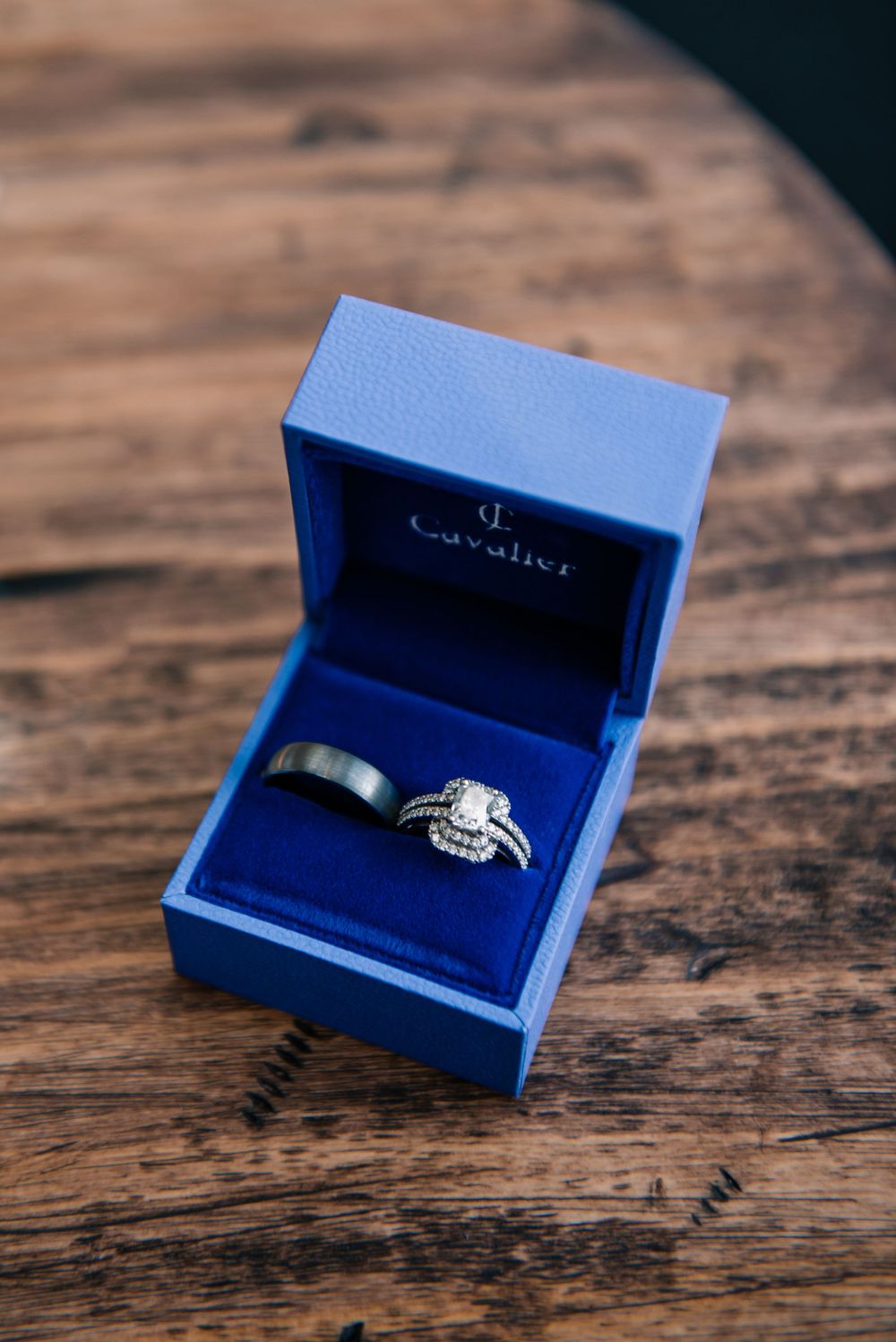 Diamond engagement ring displayed in royal blue jewelry box on wooden surface.