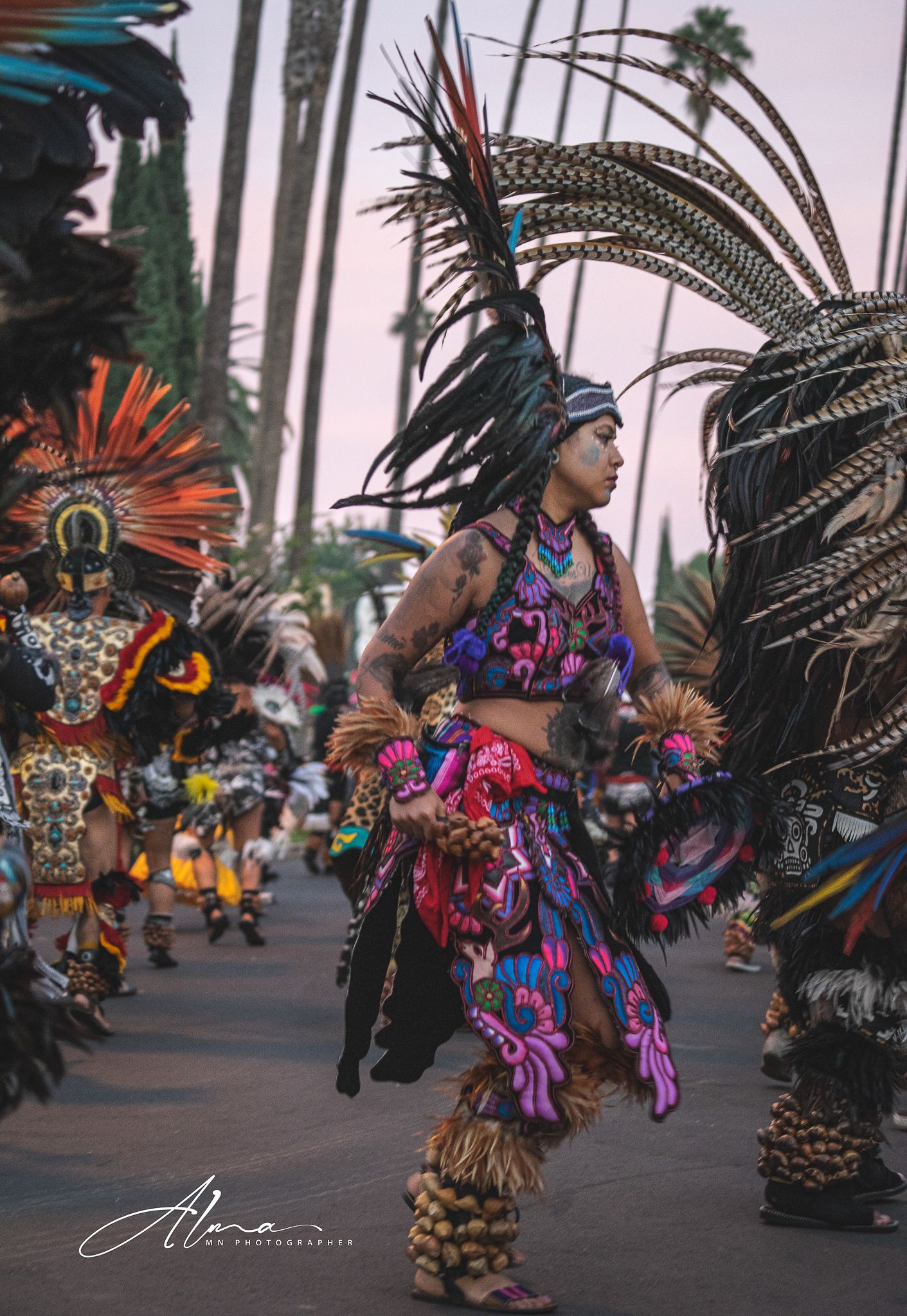 Dancer in colorful traditional Aztec regalia with large feathered headdress performs at sunset.