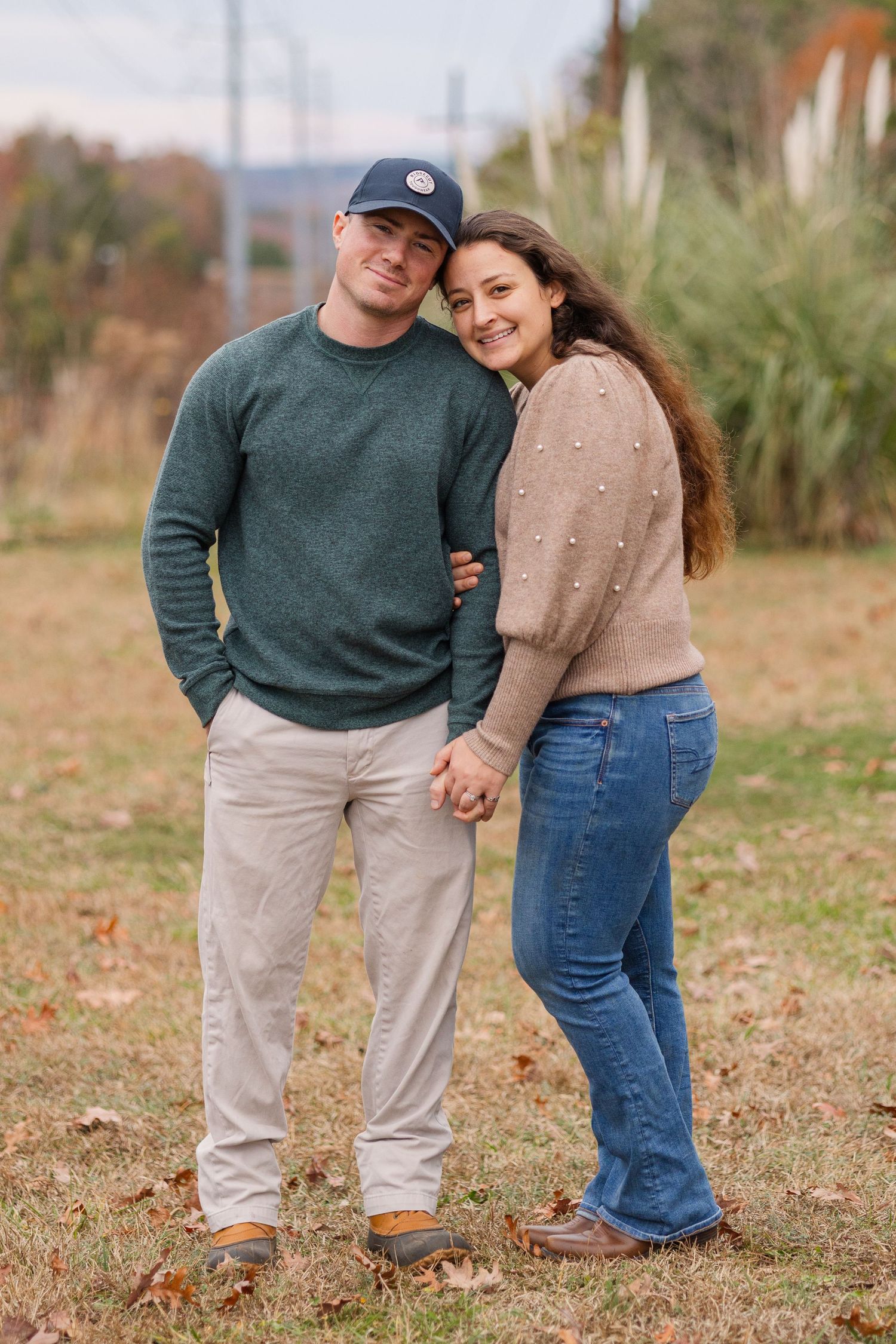 A couple in coordinating sweaters holding hands while standing in a grassy field with pampas grass.