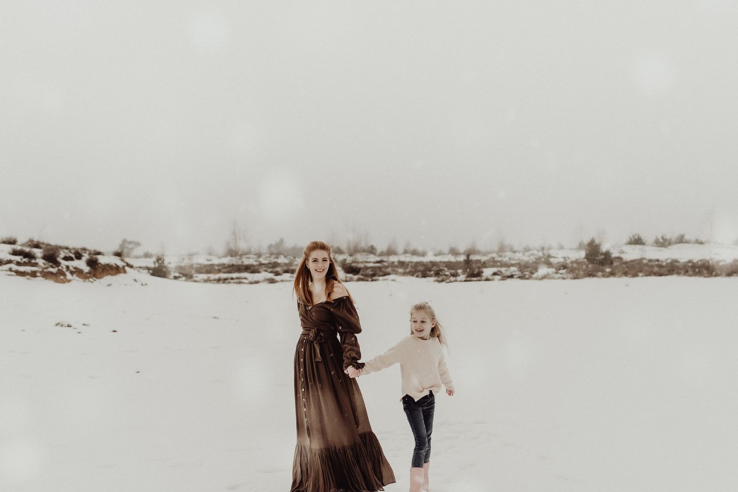 Winter maternity session in a snowy landscape with gentle movement and soft lighting.