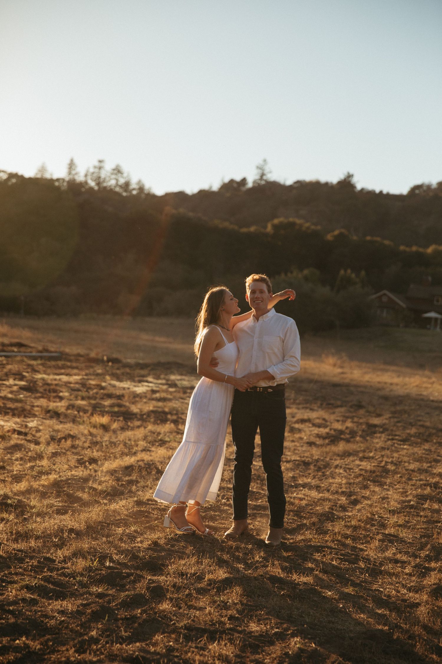 Romantic sunset engagement photo in a golden field with mountains in the background.