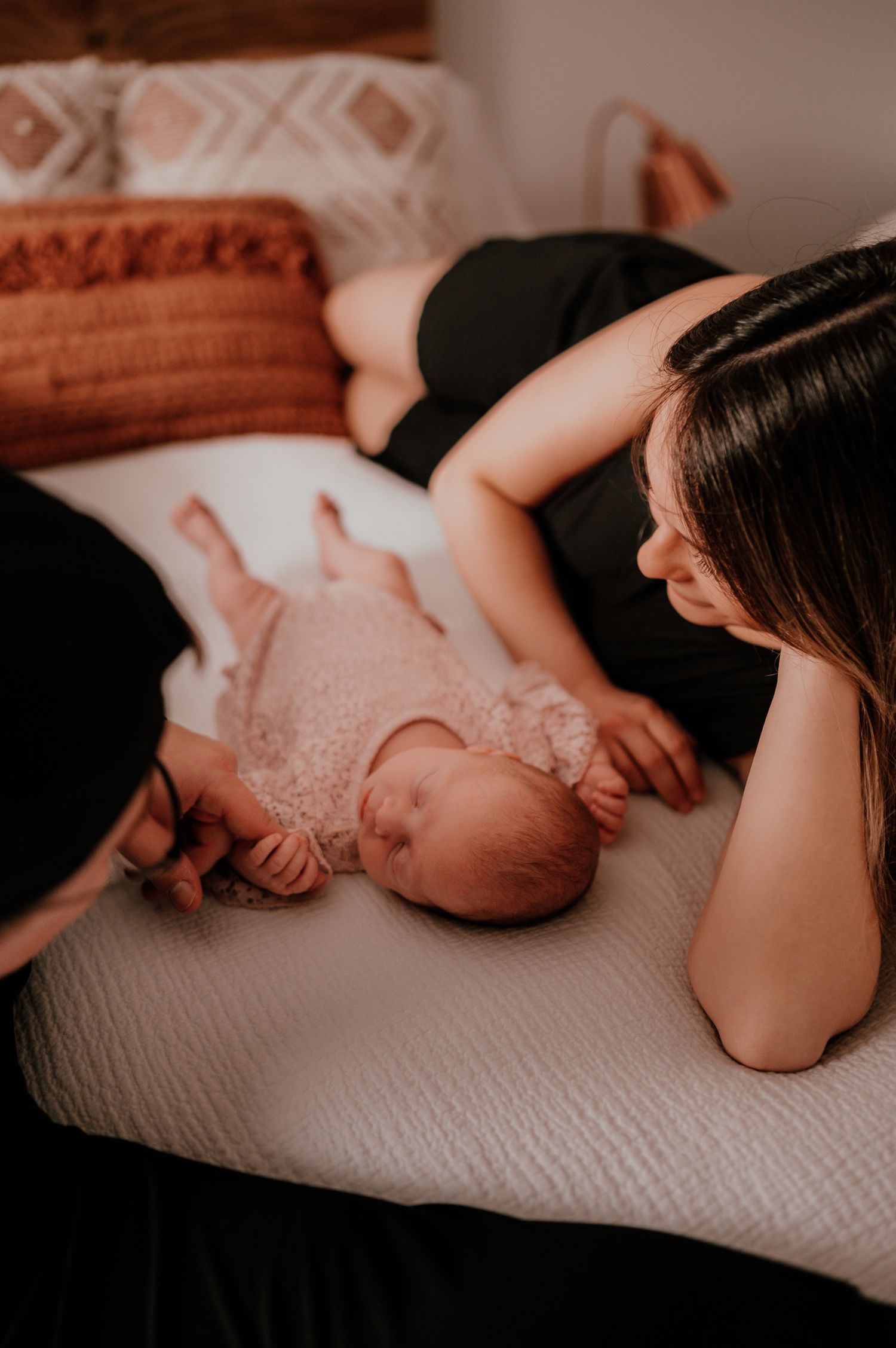 Intimate lifestyle newborn photography session on bed with soft warm lighting.