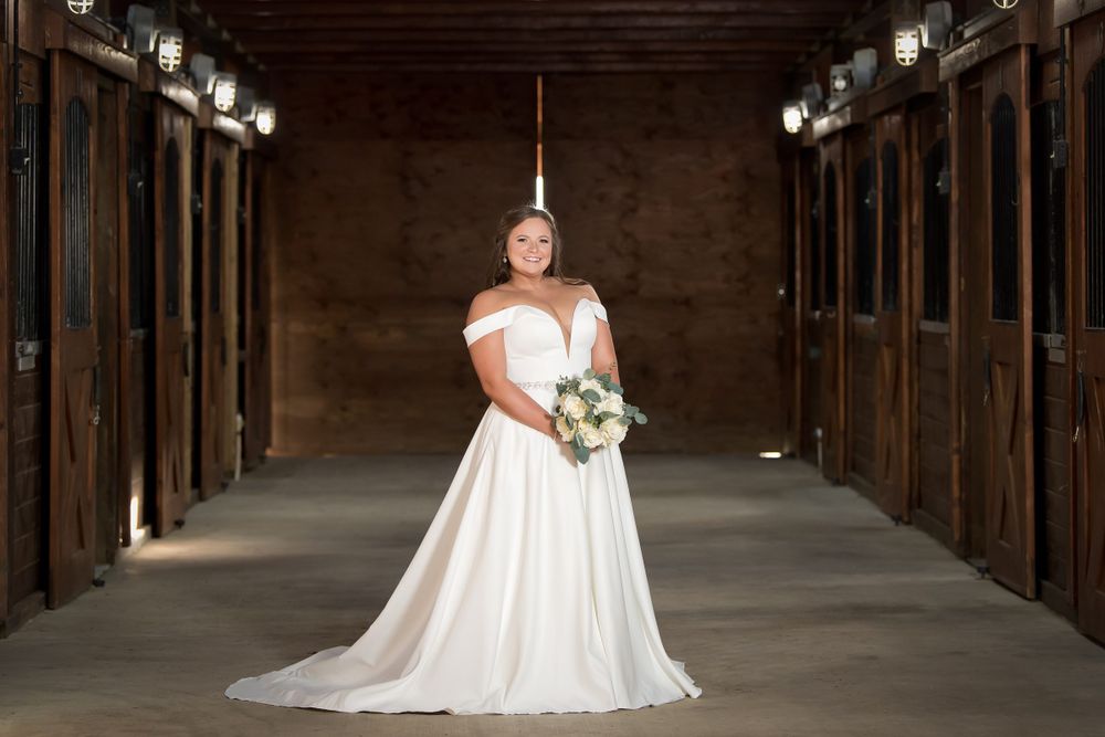 A bride in a flowing white dress poses in a dramatic barn hallway.