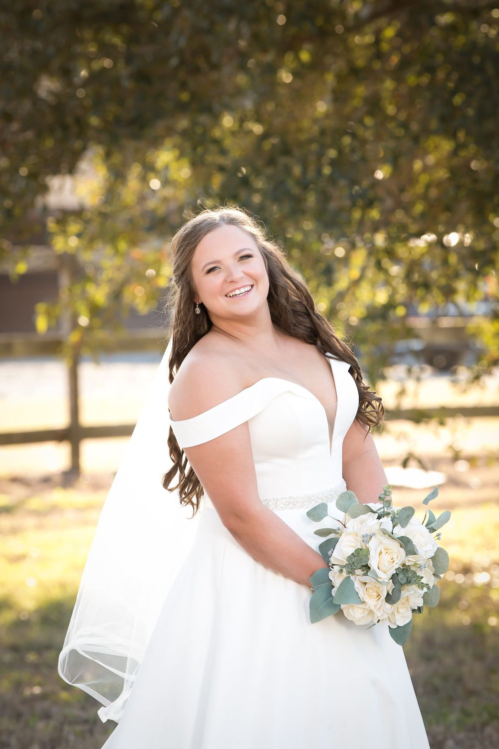 Bridal portraits in a sunlit outdoor setting with white gown and delicate bouquet against golden natural light.