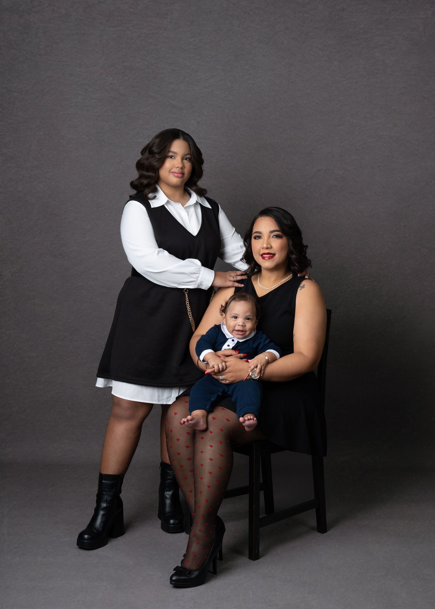 Studio portrait of three generations posing together against a dark grey background.