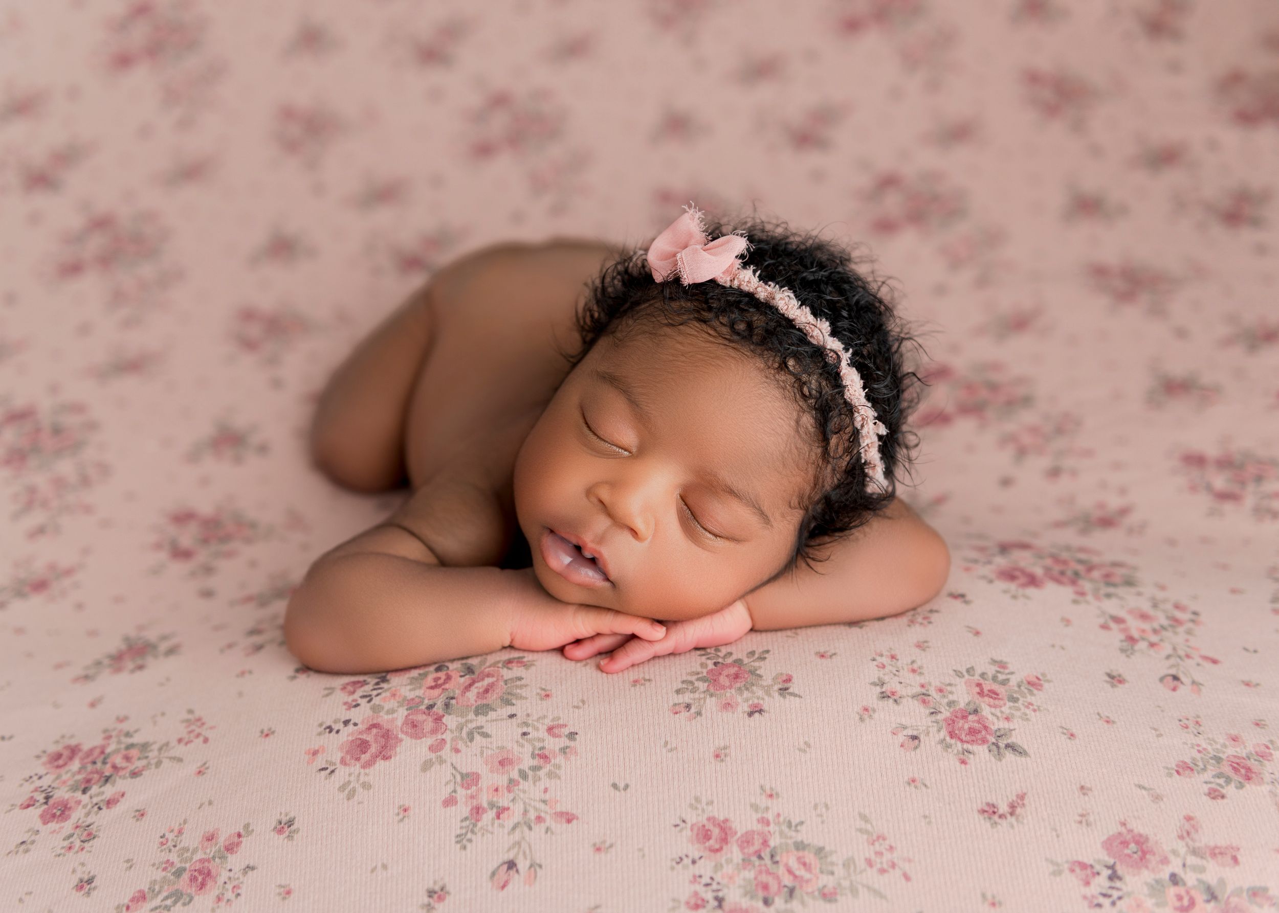 Sleeping newborn baby posed on pink floral backdrop in professional photography studio setting.