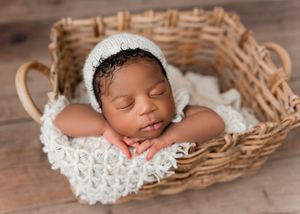 A newborn baby sleeps peacefully in a woven basket lined with white lace fabric.