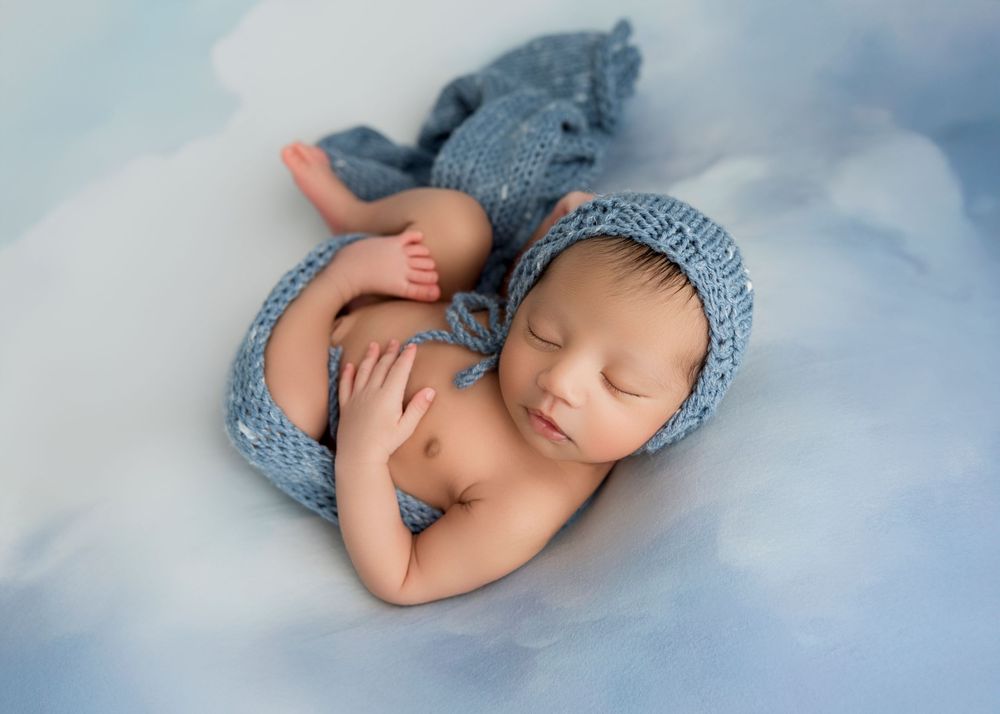 A sleeping newborn baby wearing a soft blue knit hat lies peacefully on light blue fabric in a series of gentle poses.