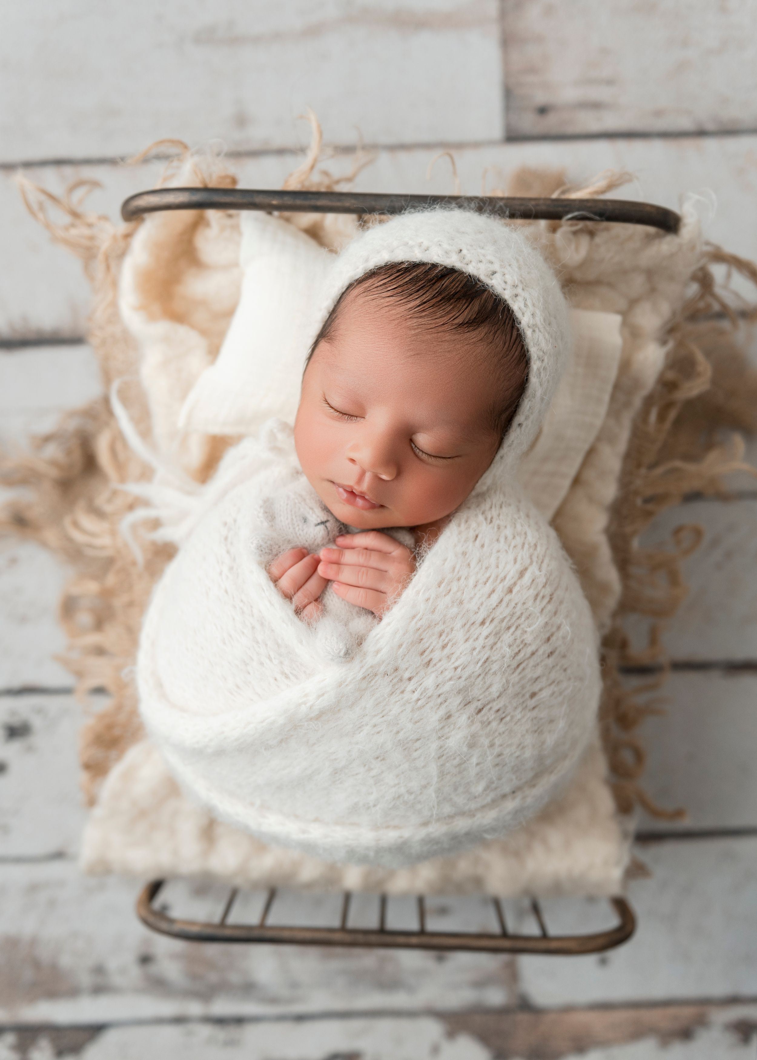 A sleeping newborn baby wrapped in a soft white knit blanket on a rustic wooden backdrop.