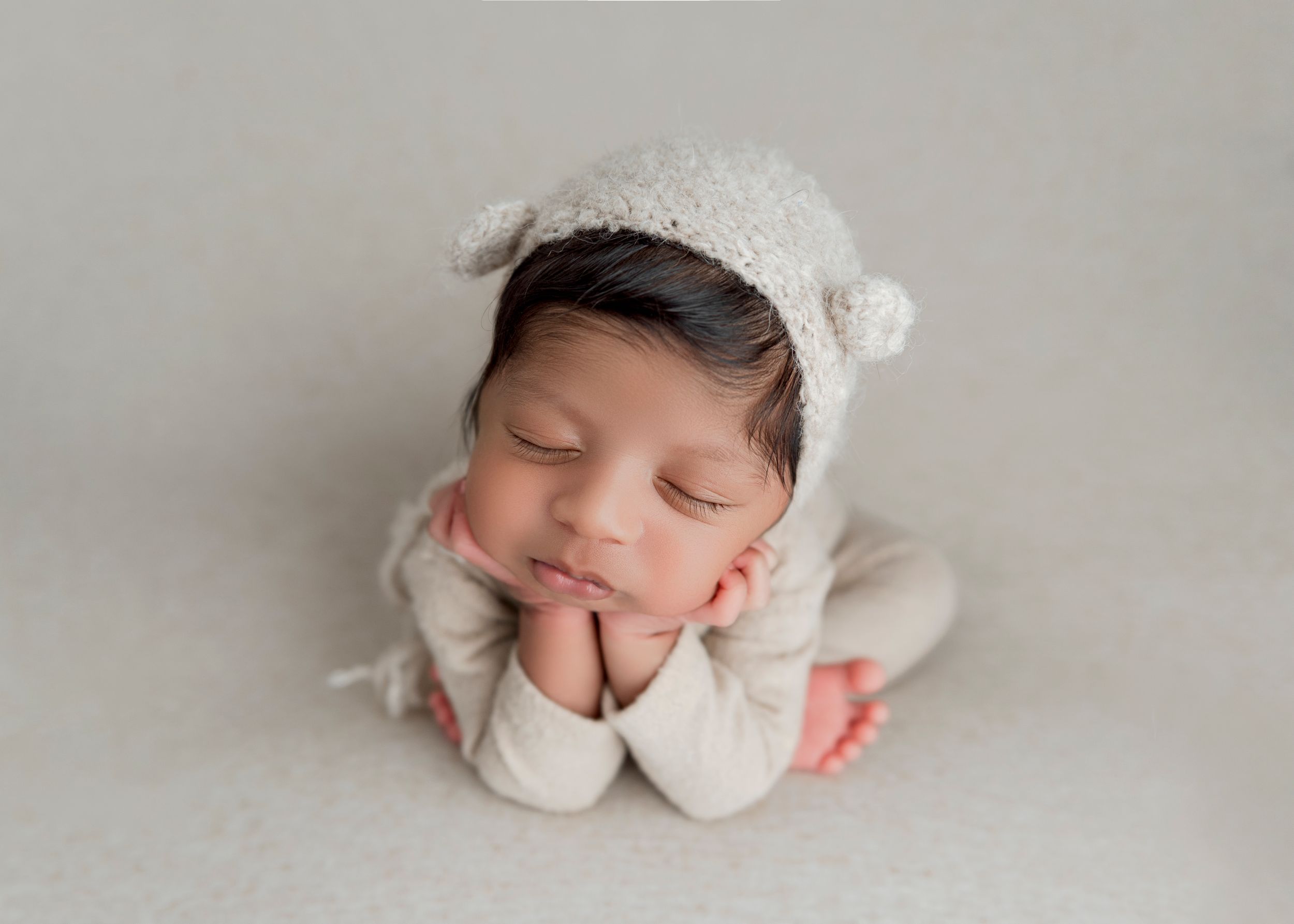 A newborn baby sleeps peacefully in a white wrap while wearing a delicate headband in a professional studio setting.