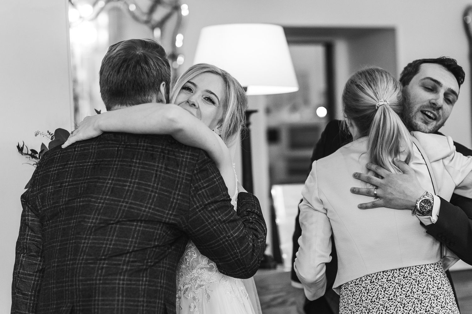 Black and white candid shot of wedding guests sharing warm hugs at reception.