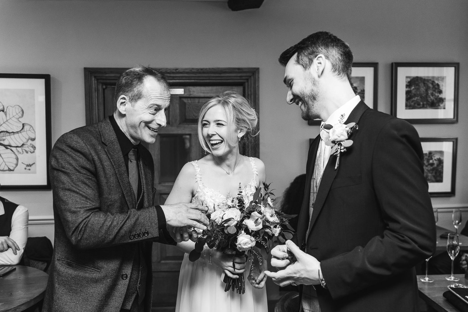 Black and white candid moment of wedding guests sharing laughter with bouquet.