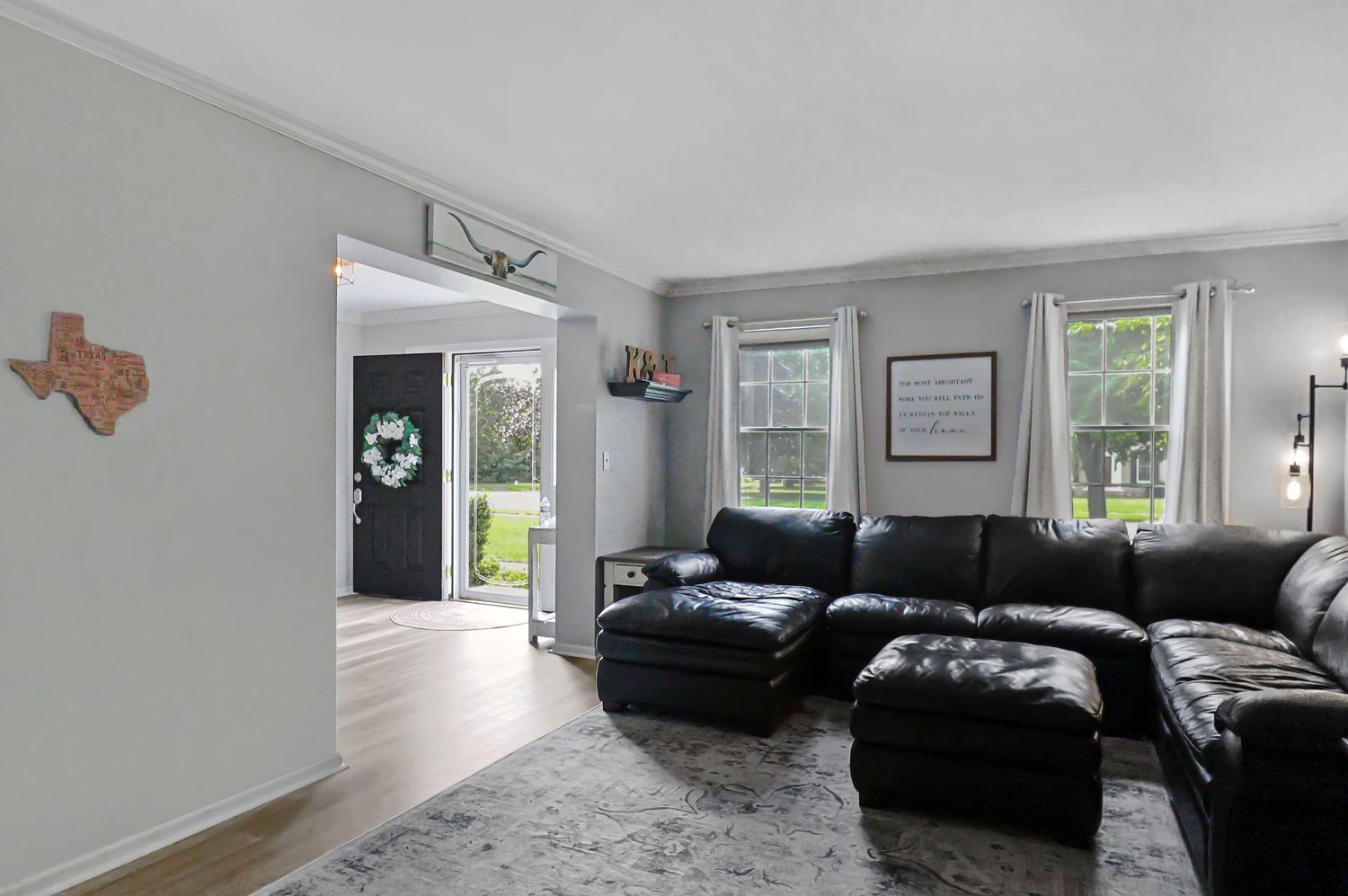 Contemporary living room with gray walls, black leather furniture, and natural light from large windows.