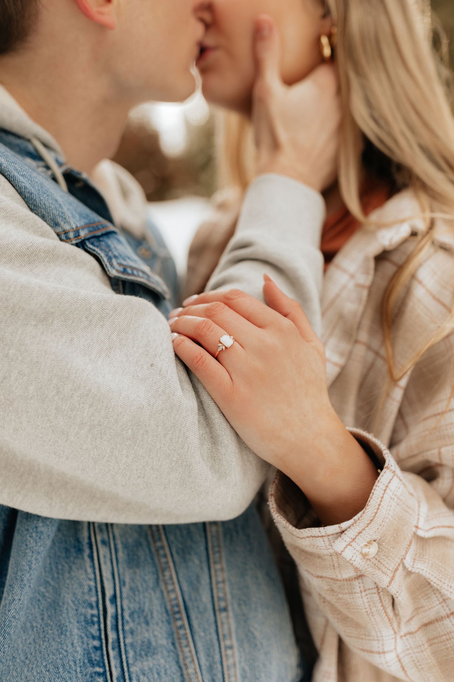Woman holding man's arm while kissing showing engagement ring