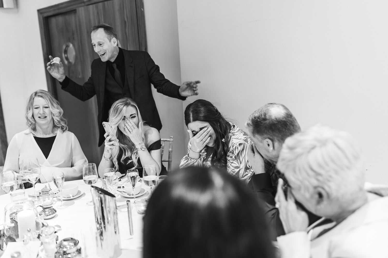 Black and white photo of guests reacting with laughter during wedding reception entertainment.