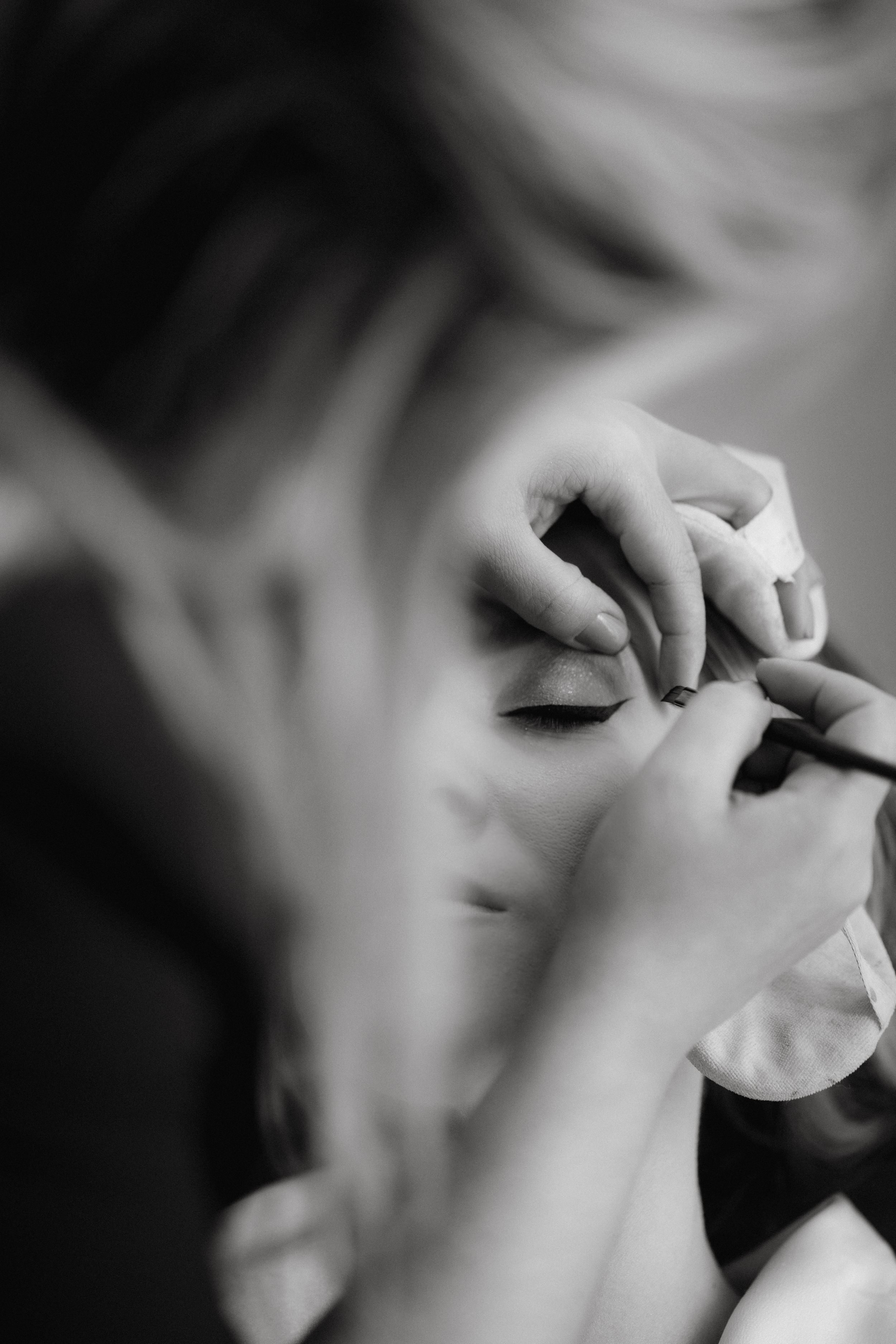 Close-up black and white photo of makeup application during wedding preparations.