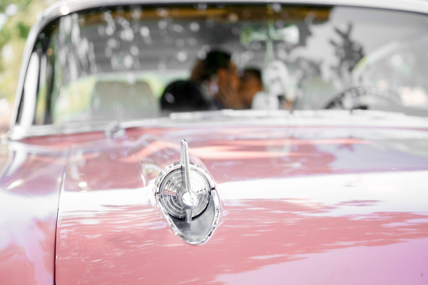 Close-up view of a vintage pink car's hood ornament with a blurred background.