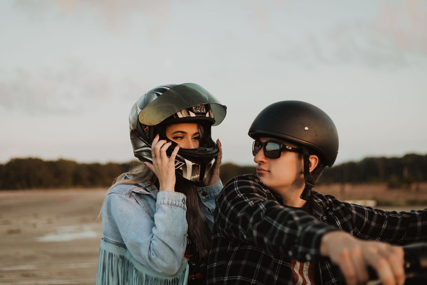 Two motorcycle riders wearing helmets talking while sitting together at sunset.