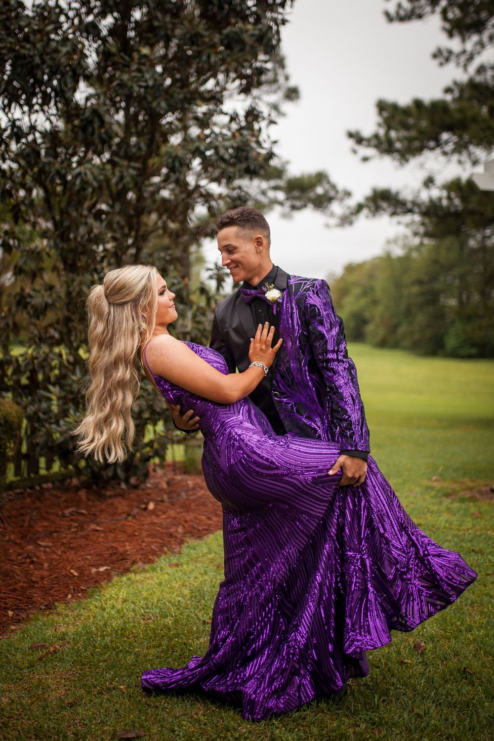 Couple dancing outdoors with woman in flowing purple gown being dipped romantically.