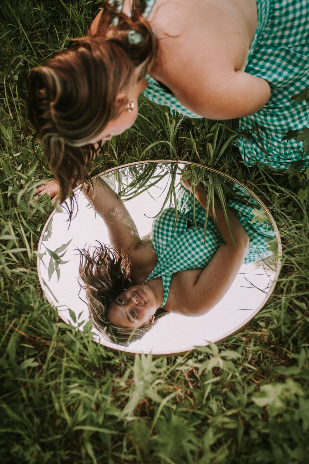 Creative mirror reflection photography in grass showing a green gingham dress.