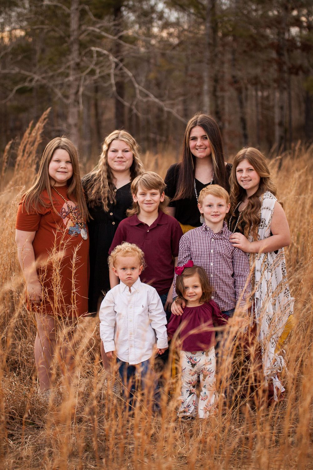 A family portrait of eight people standing together in tall autumn grass with trees in background.